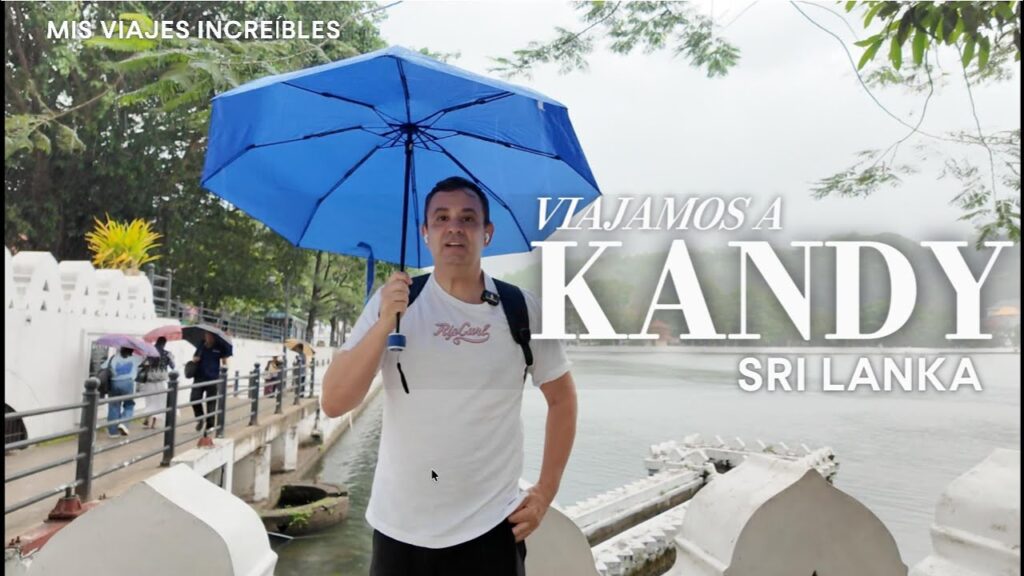 Guille (Guillermo Daniel García Lu Bello) bajo un paraguas azul junto al lago de Kandy, Sri Lanka, en un día lluvioso, con el texto "Viajamos a Kandy Sri Lanka" para Mis Viajes Increíbles.